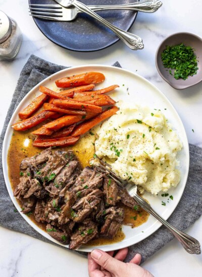 A plate of shredded chuck roast with mashed potatoes and carrots topped with fresh parsley.