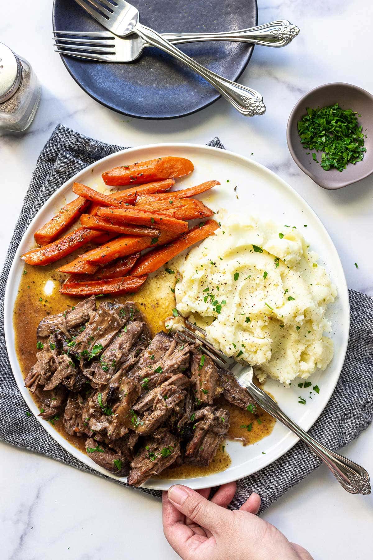 A plate of shredded chuck roast with mashed potatoes and carrots topped with fresh parsley.