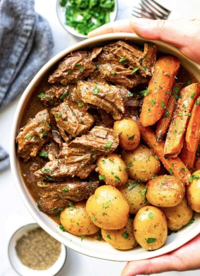 A big bowl of slow cooker pot roast with tender beef, baby yellow potatoes and carrots topped with fresh parsley.