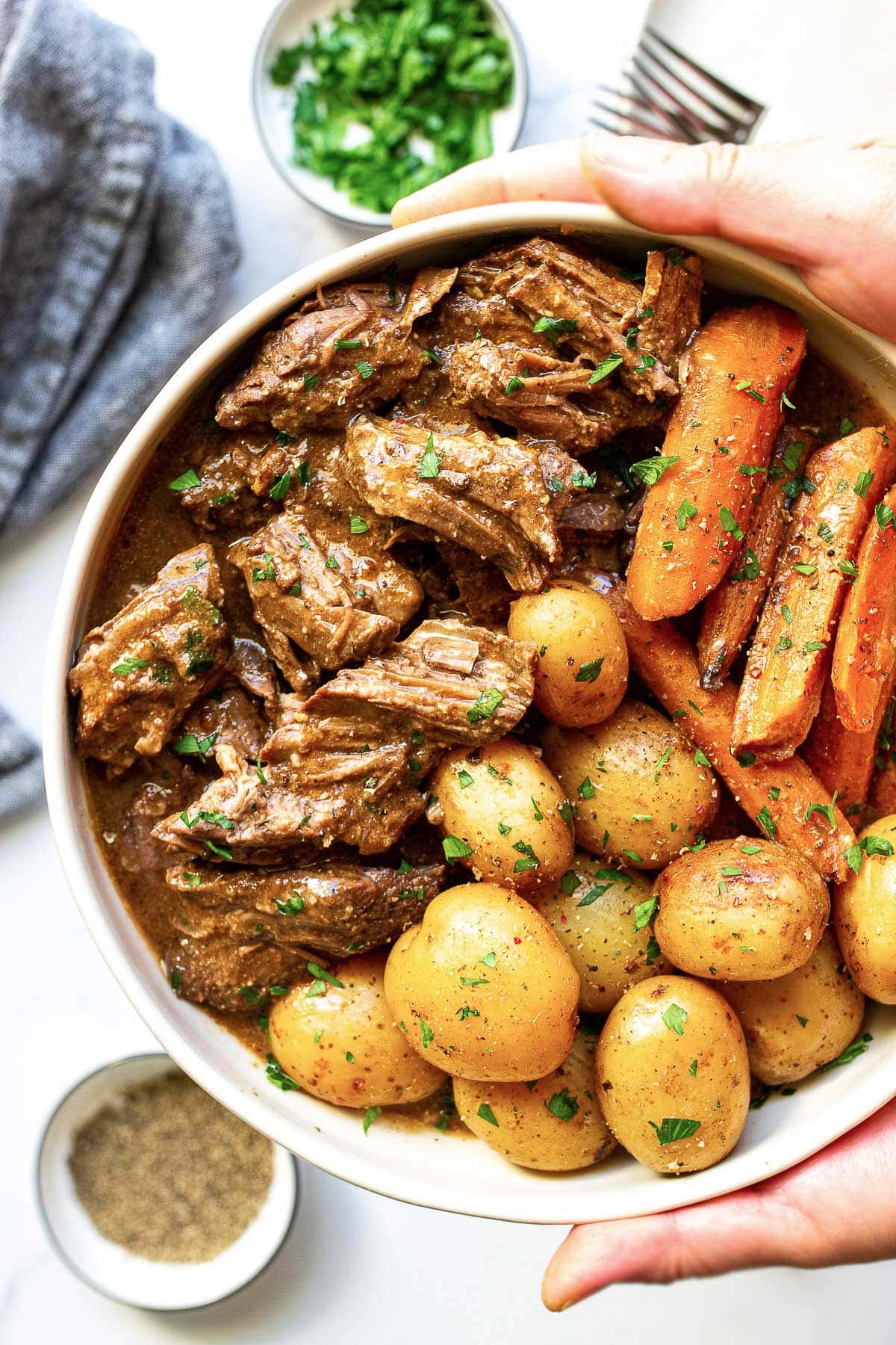 A big bowl of slow cooker pot roast with tender beef, baby yellow potatoes and carrots topped with fresh parsley.