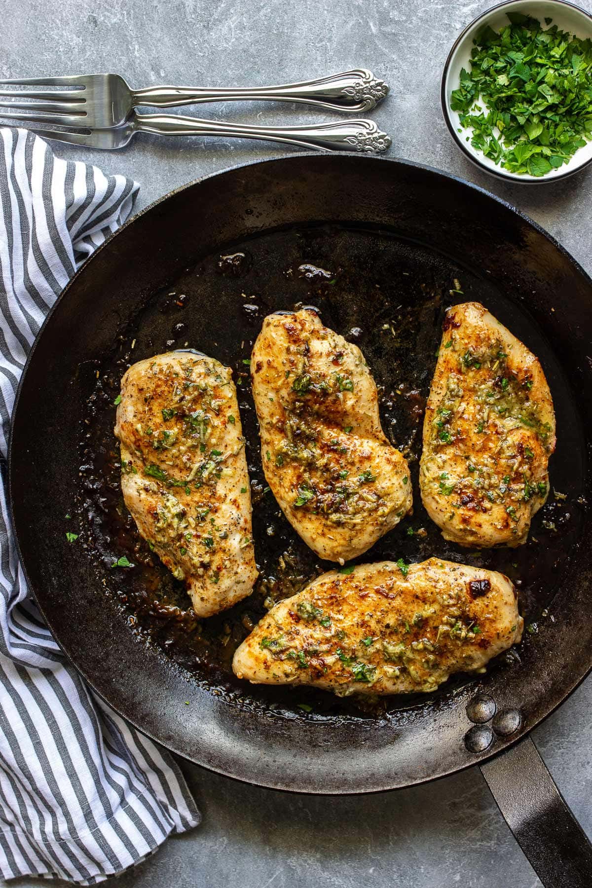 Some garlic butter baked chicken breasts in a cast iron pan topped with a herbed garlic butter sauce.