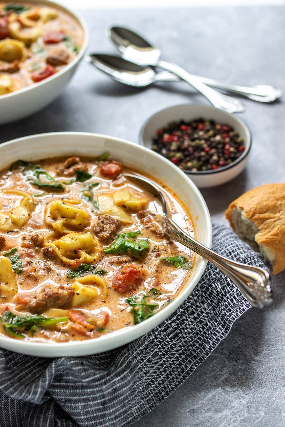 Slow cooker creamy tortellini soup in a white bowl with torn, crusty bread.