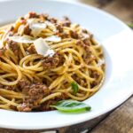 Slow cooker spaghetti Bolognese on a white plate with shaved Parmesan cheese.