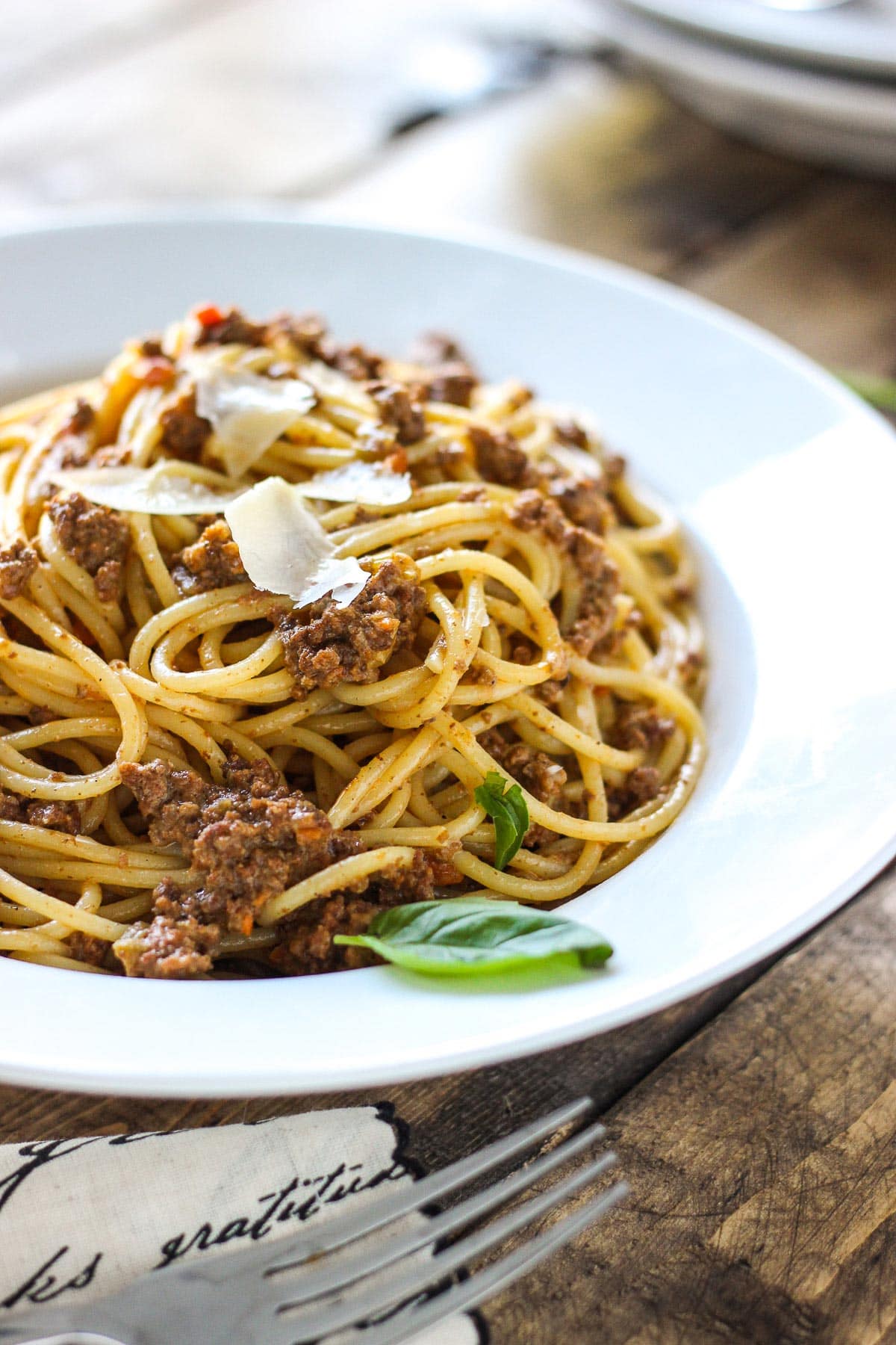 A bowl of slow cooker spaghetti Bolognese on a white plate with shaved Parmesan cheese.