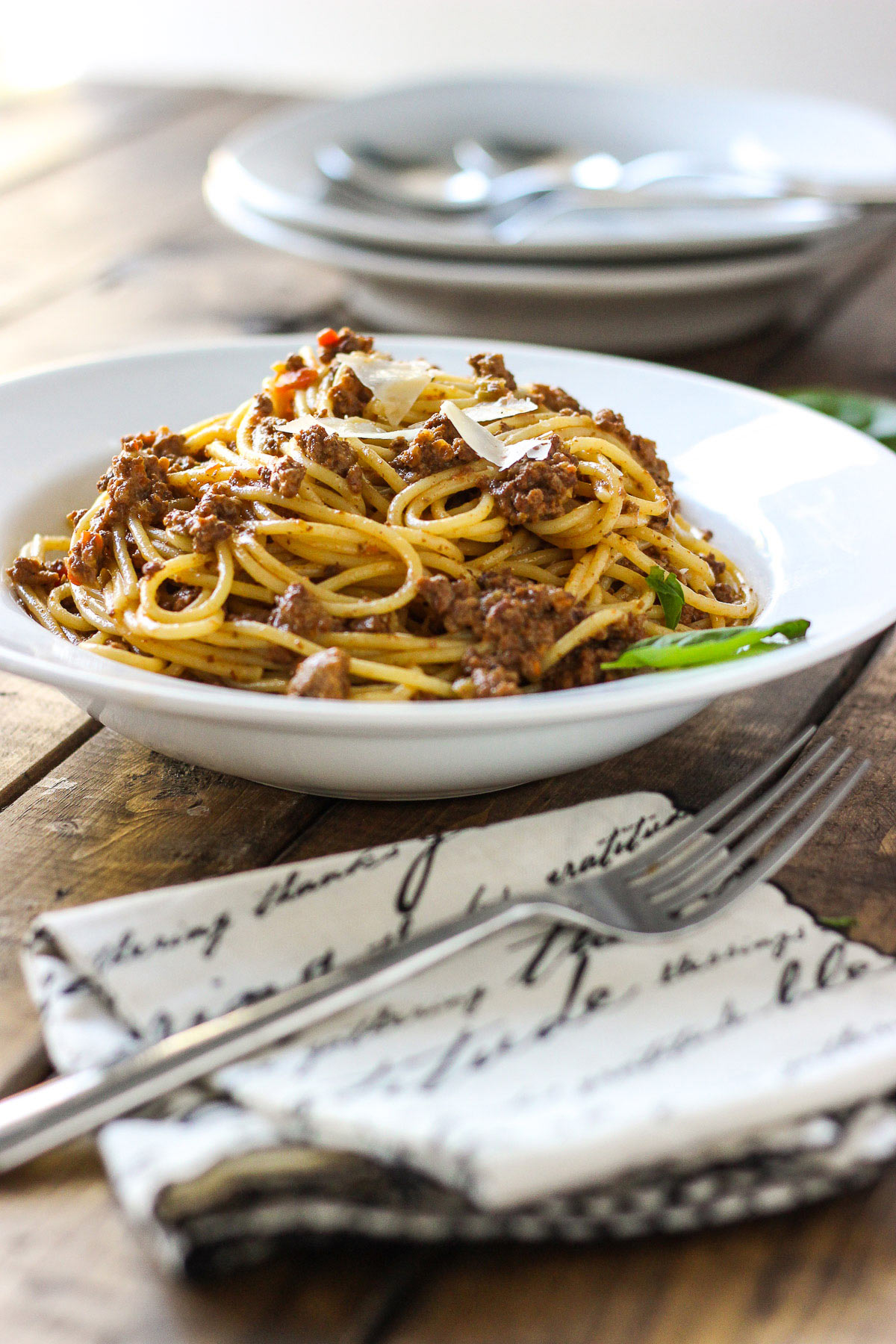 Slow cooker spaghetti Bolognese on a white plate with shaved Parmesan cheese.