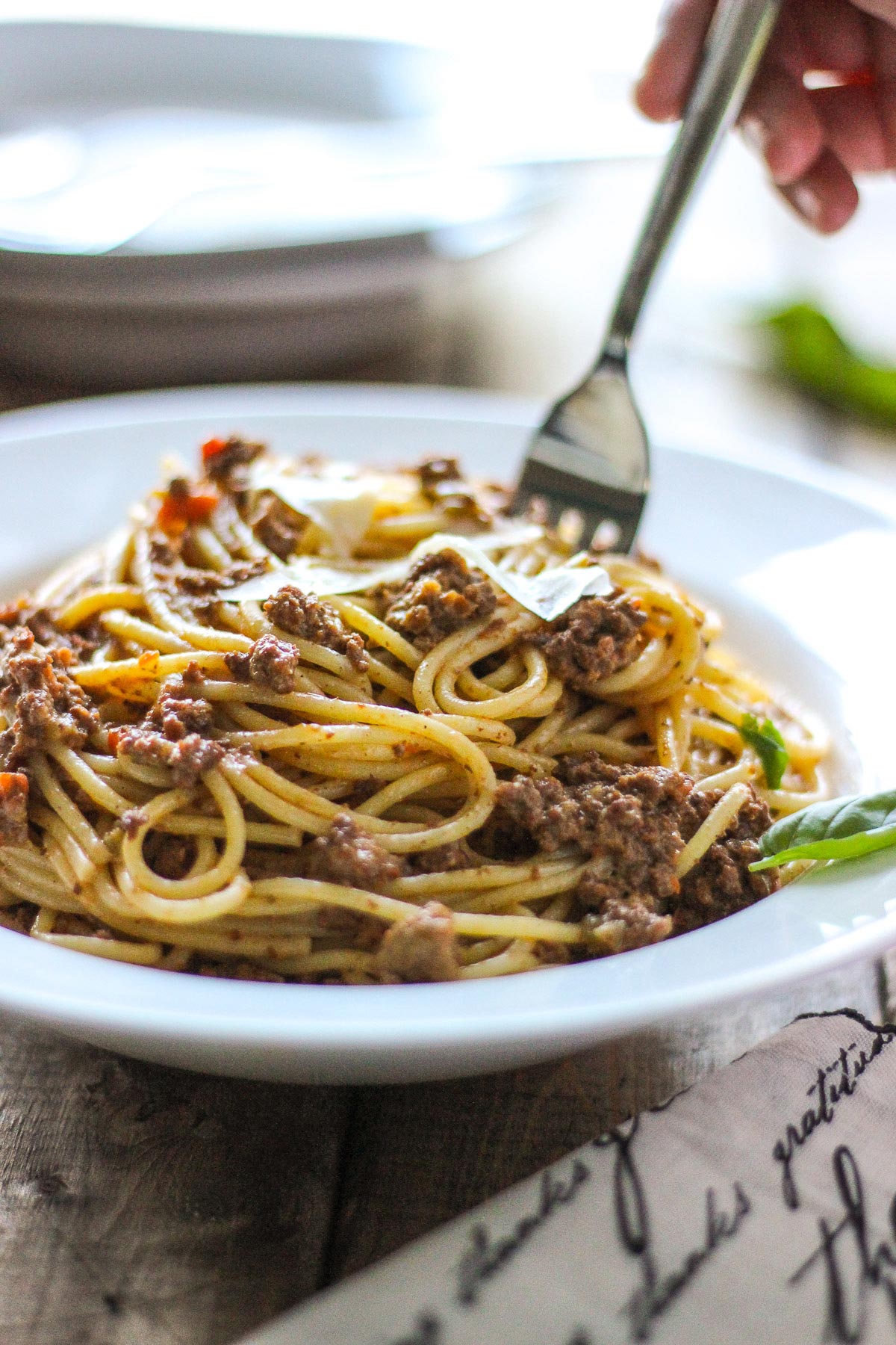 Slow cooker spaghetti Bolognese on a white plate with shaved Parmesan cheese.