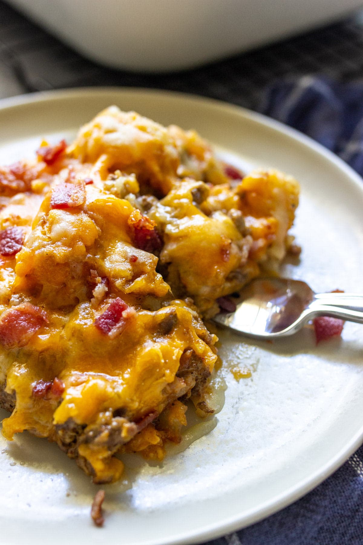 Close up photo of bacon cheeseburger tater tot casserole on a white plate.