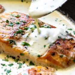 A close up shot of sauce drizzled over creamy garlic butter salmon.