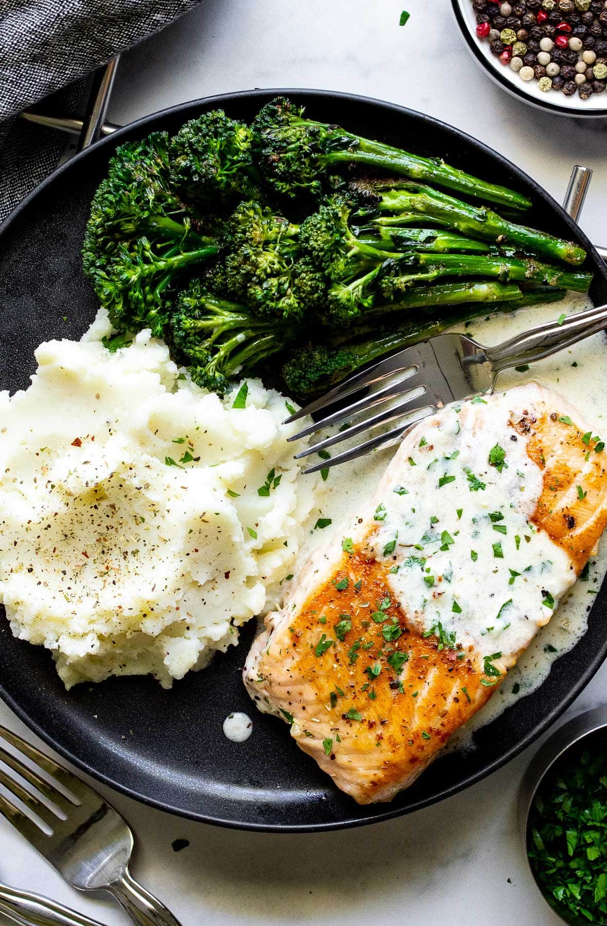 A black plate with creamy garlic butter salmon and broccolini and mashed potatoes on the side.