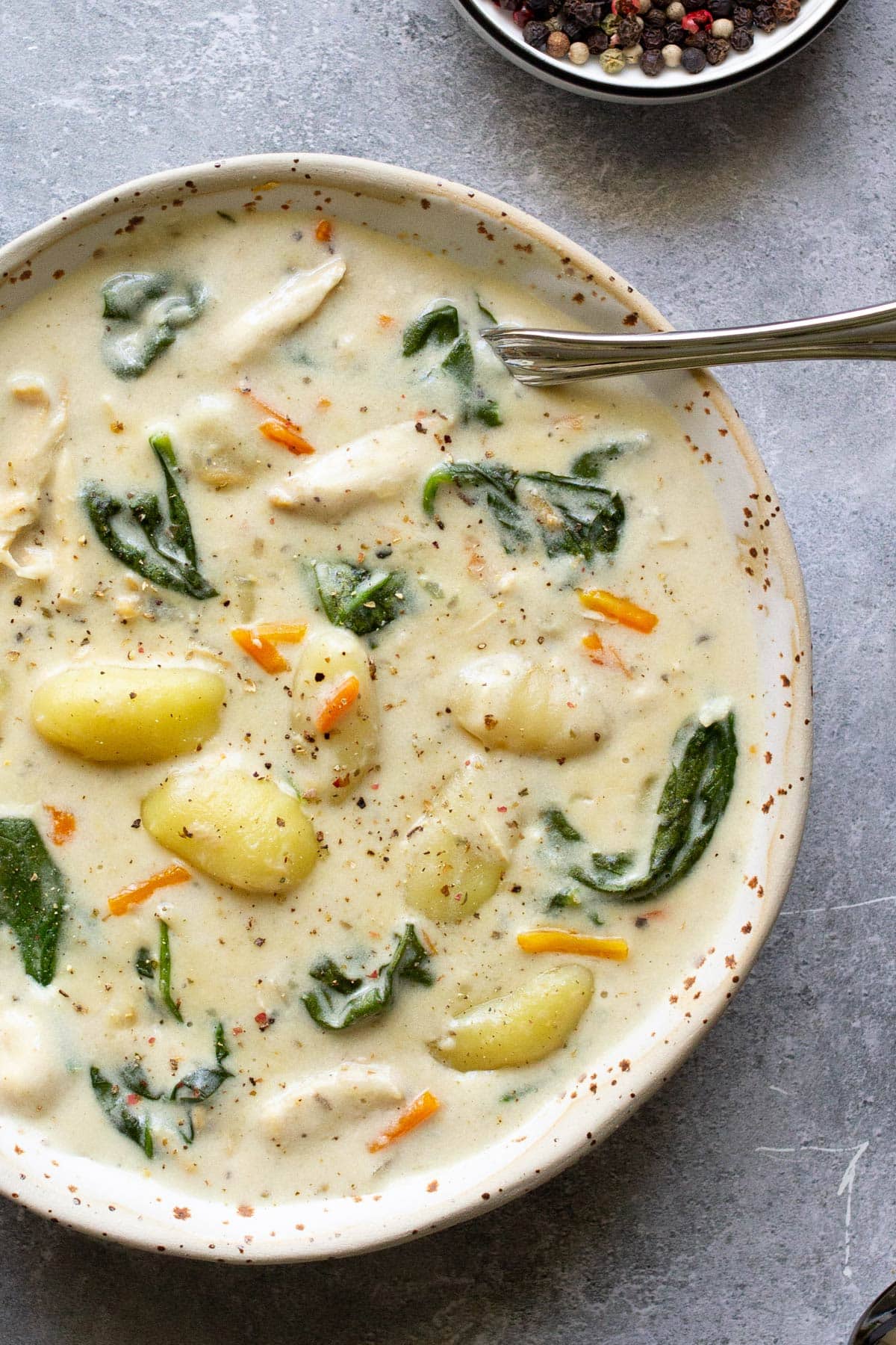 A bowl of slow cooker chicken gnocchi soup topped with cracked black pepper.