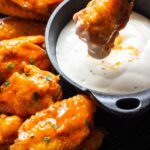 Air fryer buffalo chicken wings on a black plate with ranch dressing in a mini cast iron dip bowl.