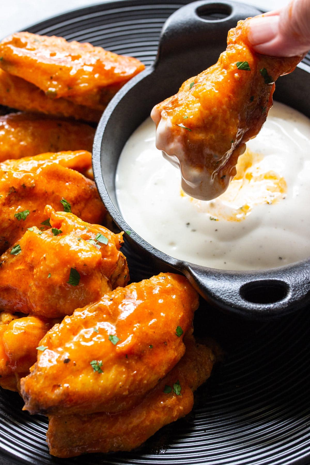 Air fryer buffalo chicken wings on a black plate with ranch dressing in a mini cast iron dip bowl.