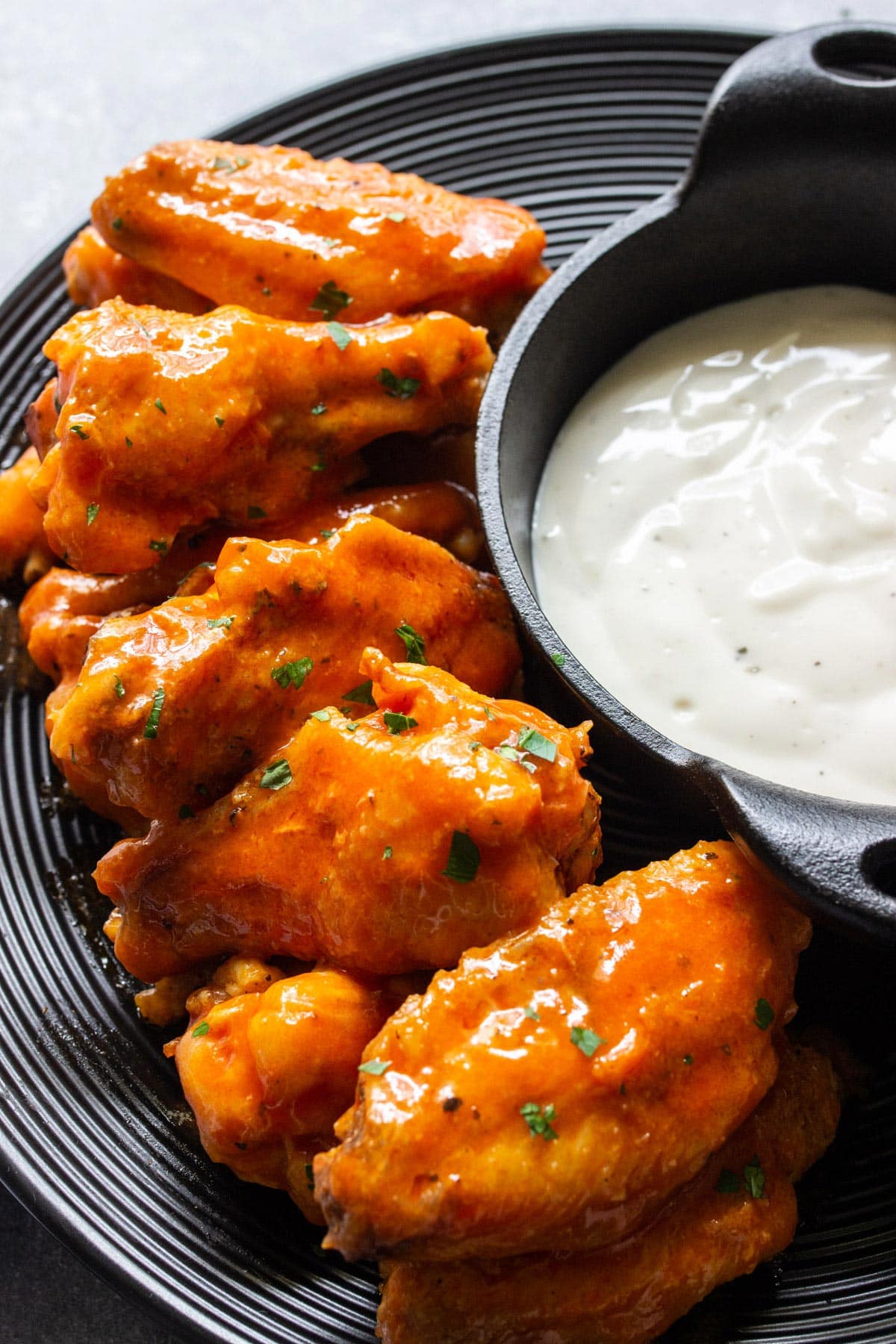 Air fryer buffalo chicken wings on a black plate with ranch dressing in a mini cast iron dip bowl.