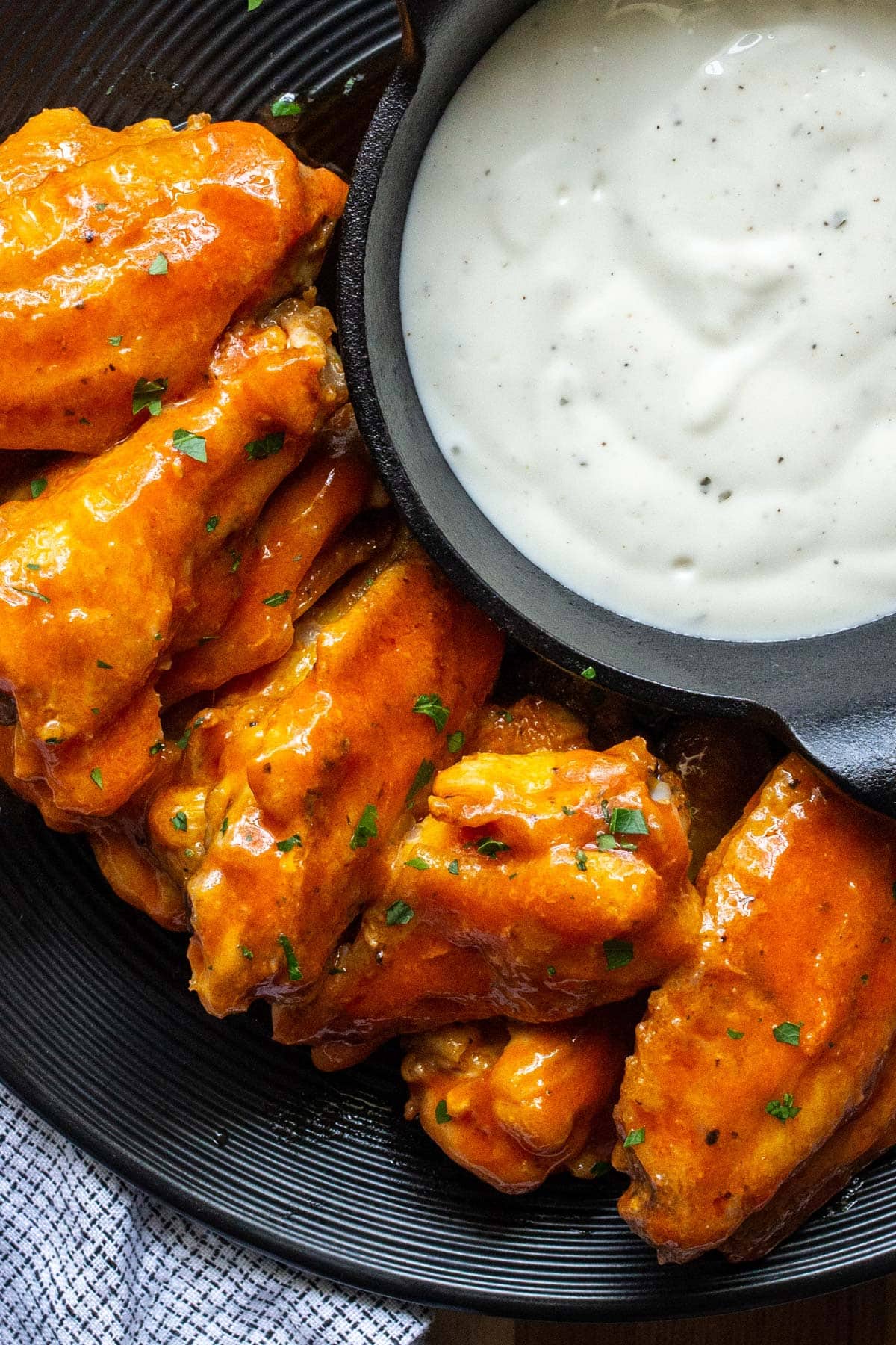 Air fryer buffalo chicken wings on a black plate with ranch dressing in a mini cast iron dip bowl.