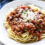 Pasta on a white plate topped with homemade spaghetti sauce, Parmesan cheese and parsley.