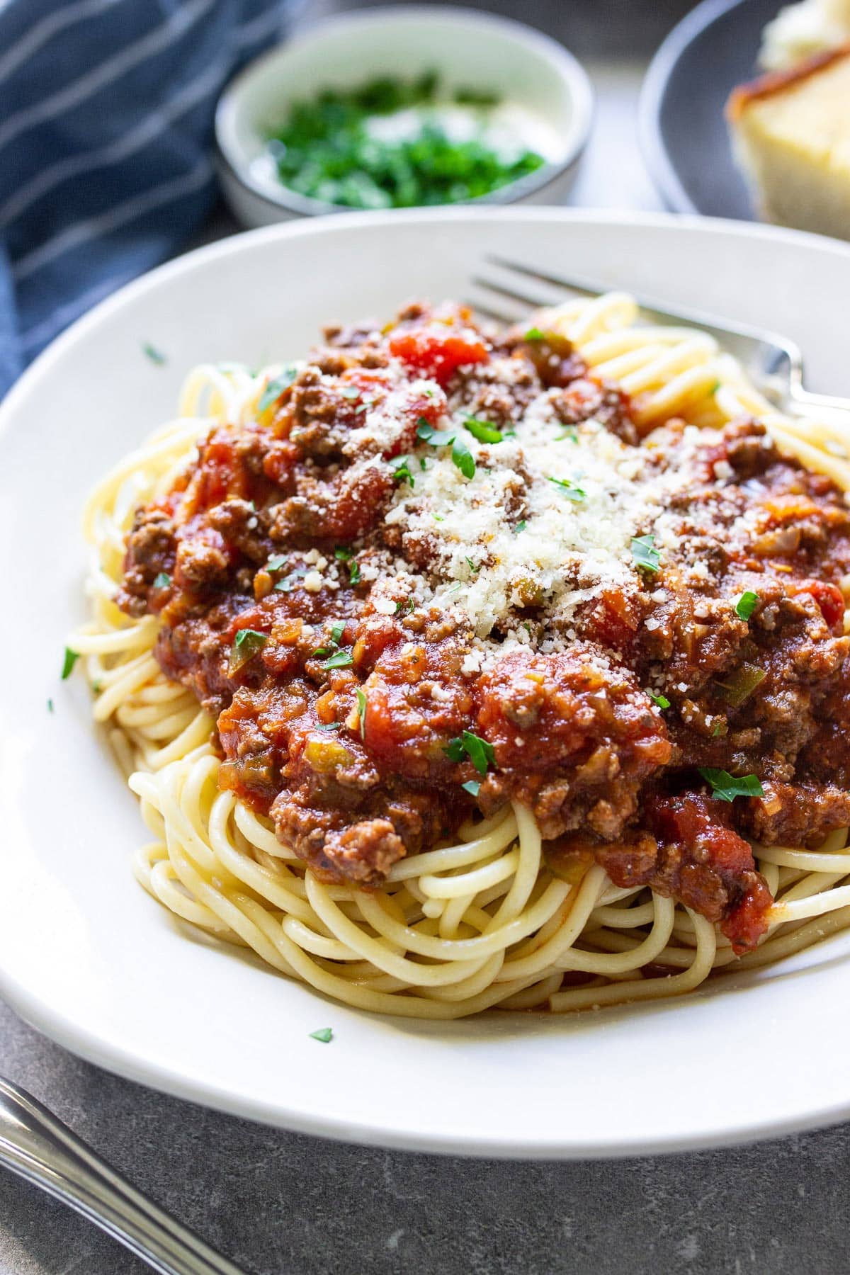 Pasta on a white plate topped with homemade spaghetti sauce, Parmesan cheese and parsley.