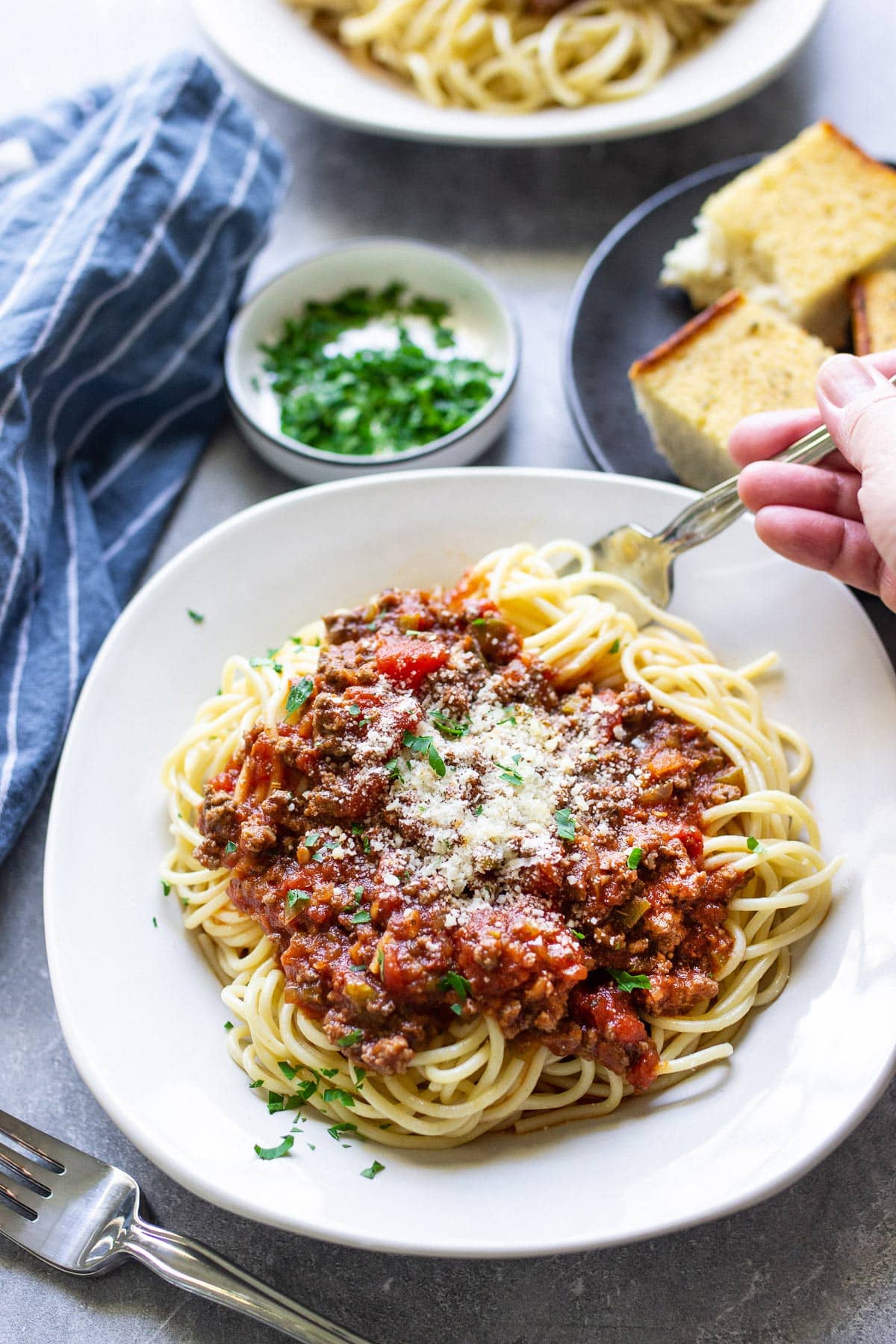 Pasta on a white plate topped with homemade spaghetti sauce, Parmesan cheese and parsley.