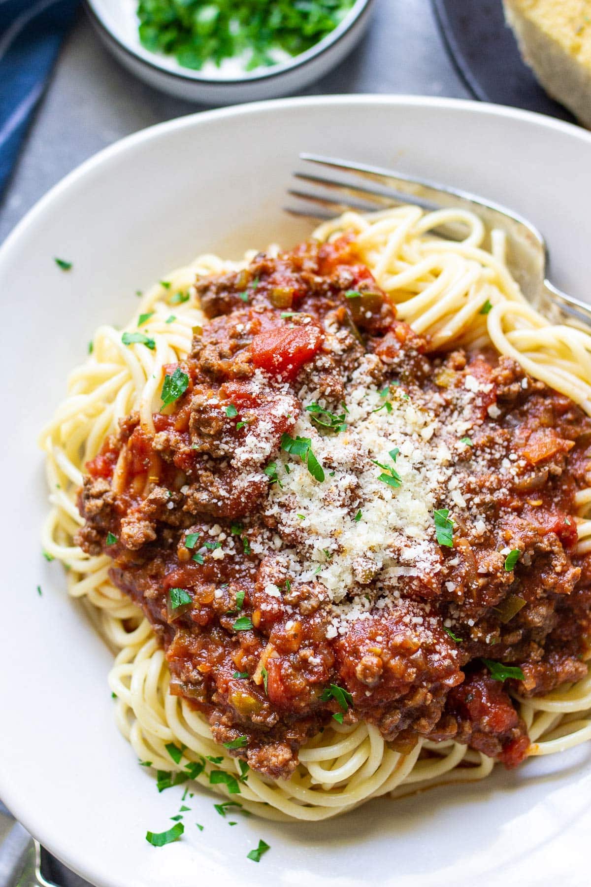 Pasta on a white plate topped with homemade spaghetti sauce, Parmesan cheese and parsley.