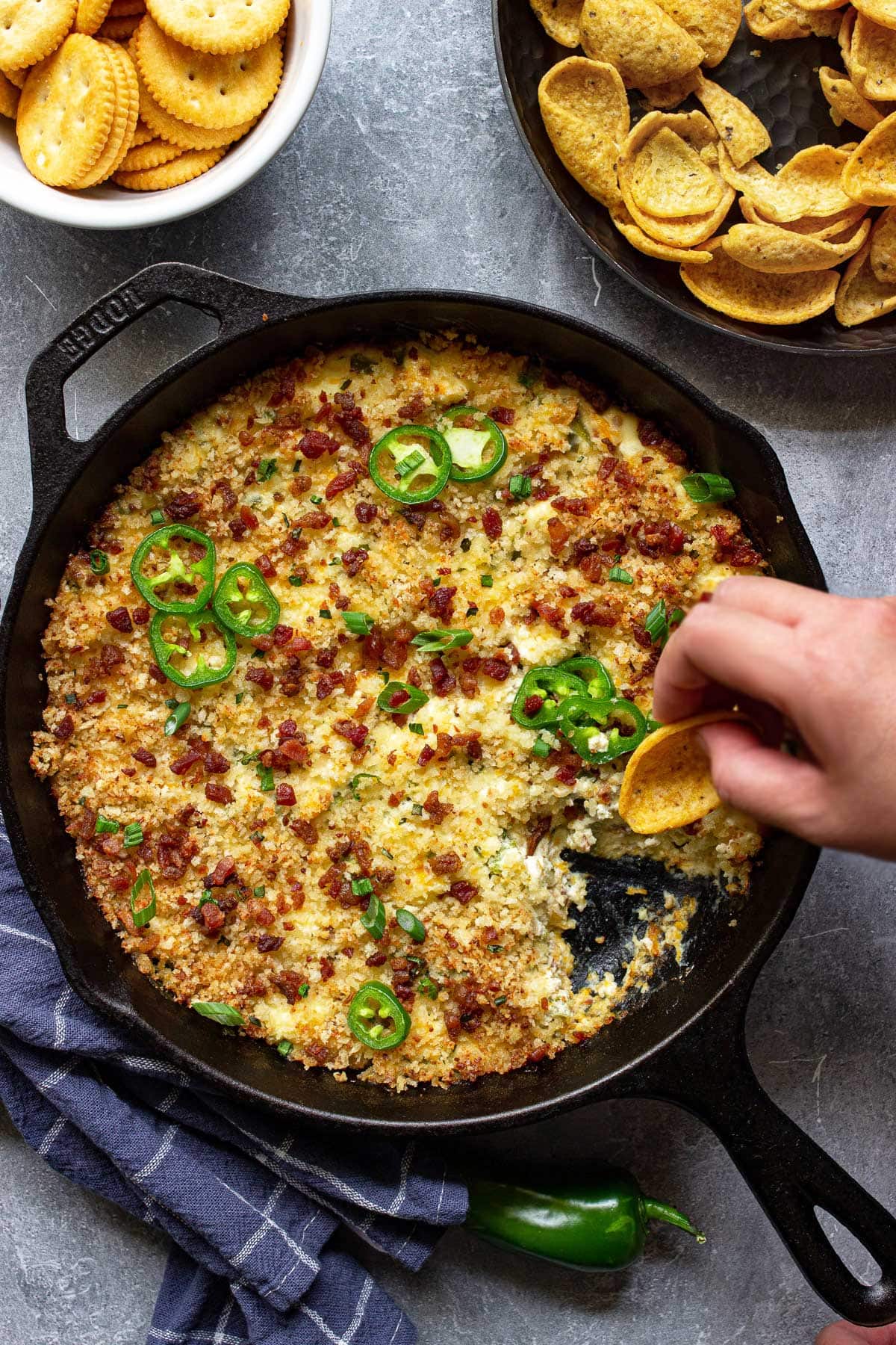 Jalapeno popper dip in a cast iron pan topped with jalapeno slices, bacon bits and green onions.