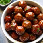 Slow cooker grape jelly meatballs stacked in a wide white bowl and topped with fresh parsley.