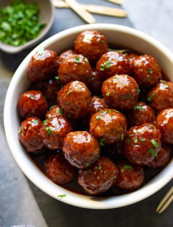 Slow cooker grape jelly meatballs stacked in a wide white bowl and topped with fresh parsley.