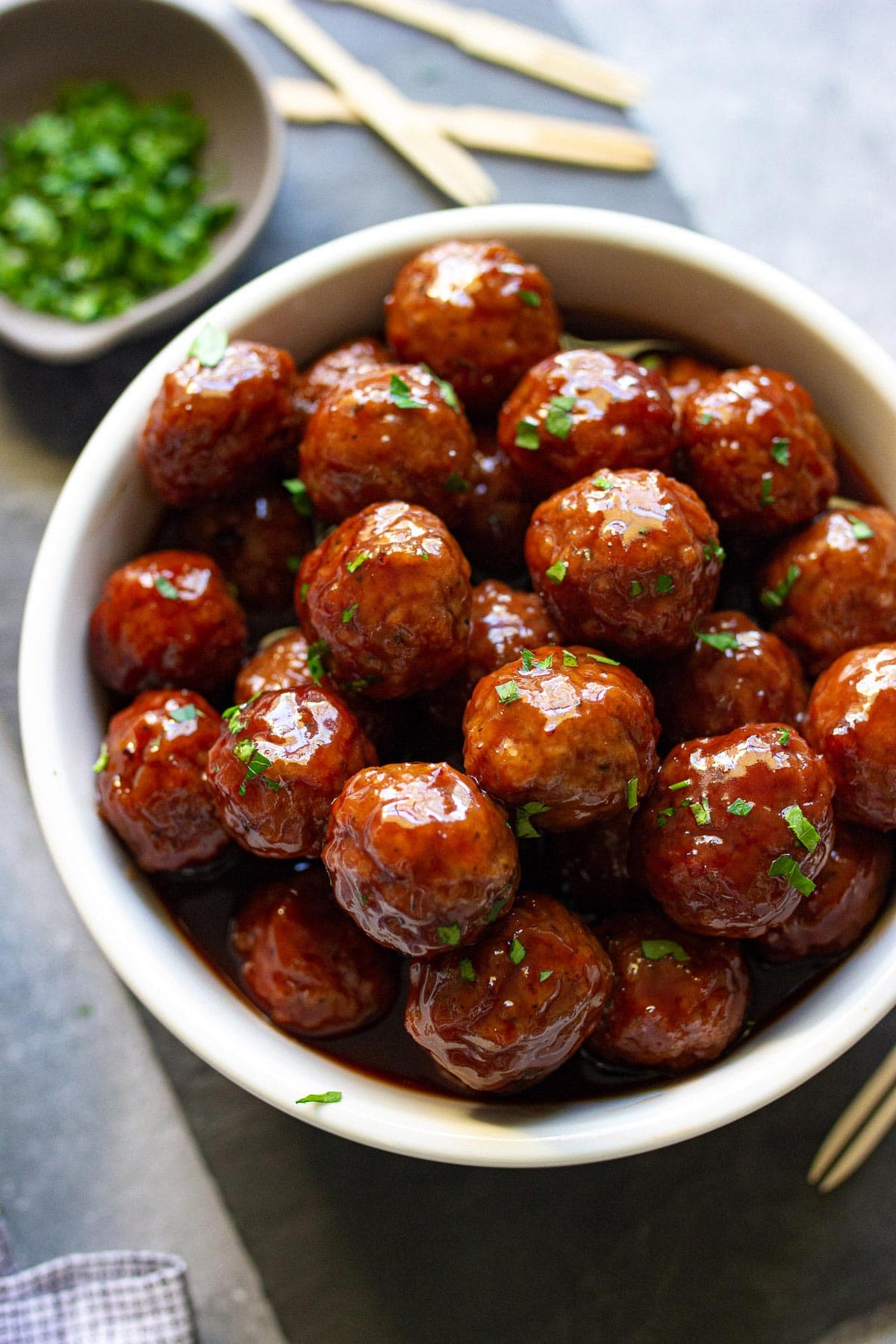 Slow cooker grape jelly meatballs stacked in a wide white bowl and topped with fresh parsley.