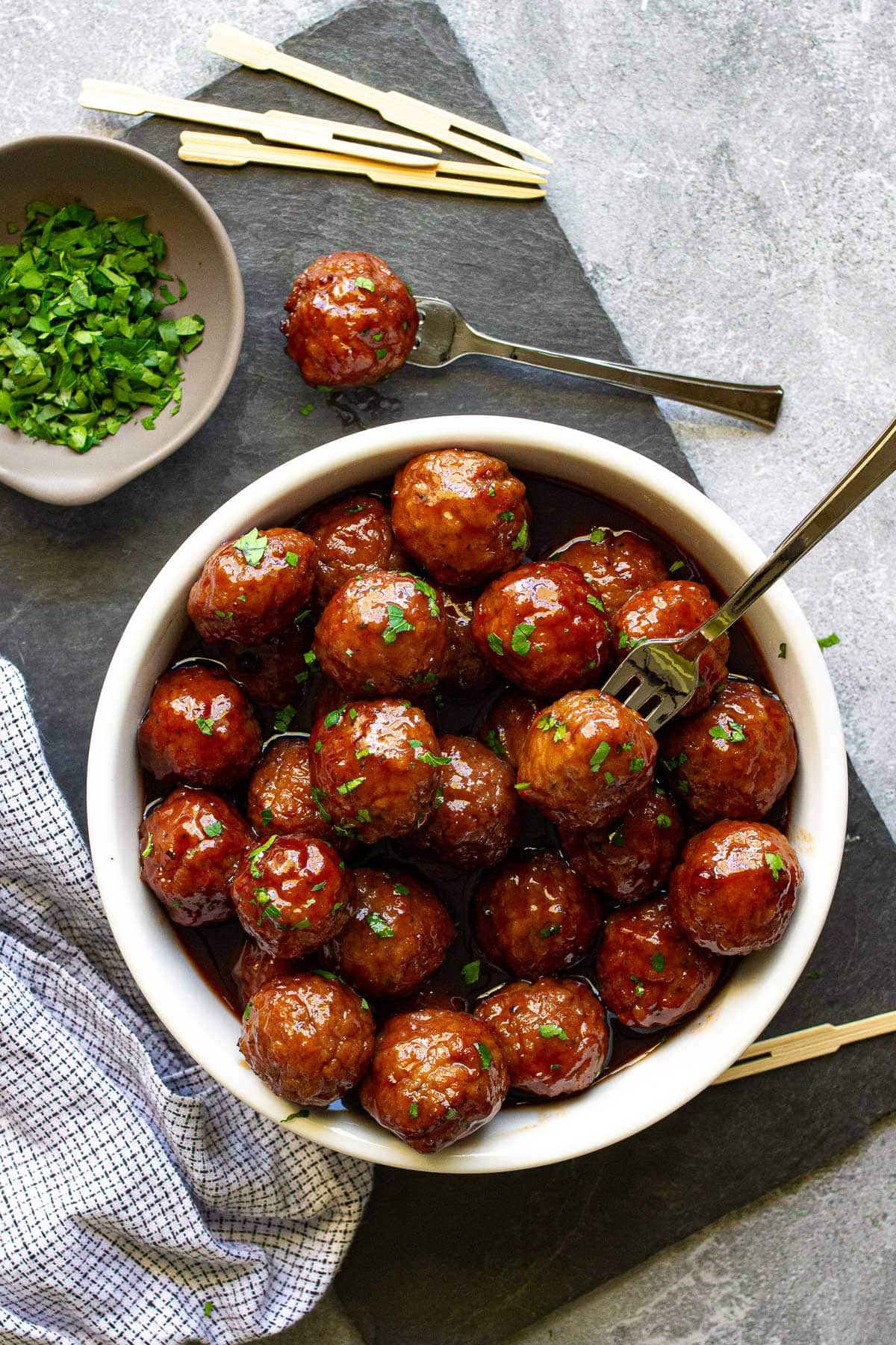 Slow cooker grape jelly meatballs stacked in a wide white bowl and topped with fresh parsley.