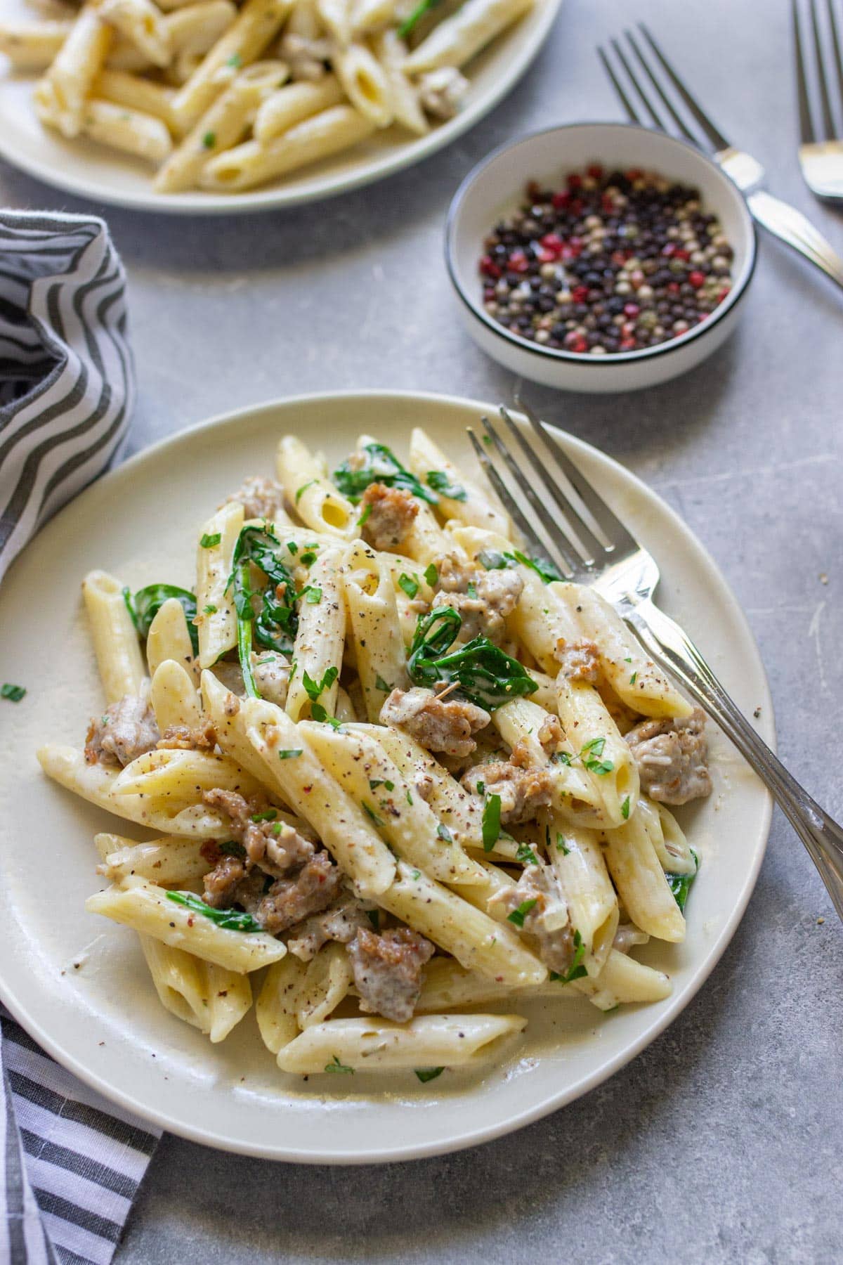 Two servings of creamy sausage pasta on cream colored plates.