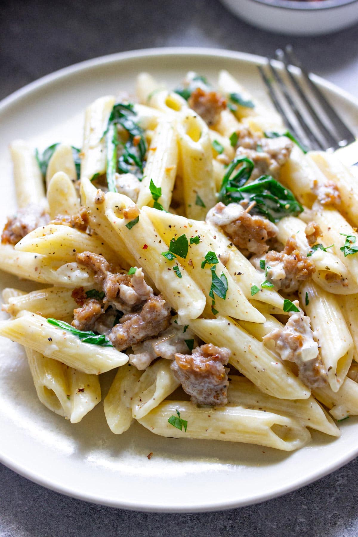 Close up of creamy sausage pasta on a plate topped with fresh parsley and cracked black pepper.