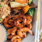 A plate full of hibachi shrimp, hibachi rice and hibachi vegetables with a side of yum yum sauce.