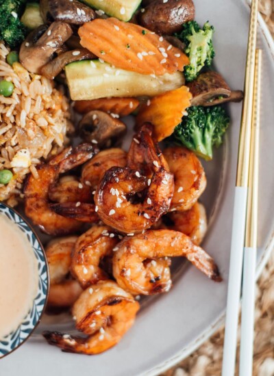 A plate full of hibachi shrimp, hibachi rice and hibachi vegetables with a side of yum yum sauce.