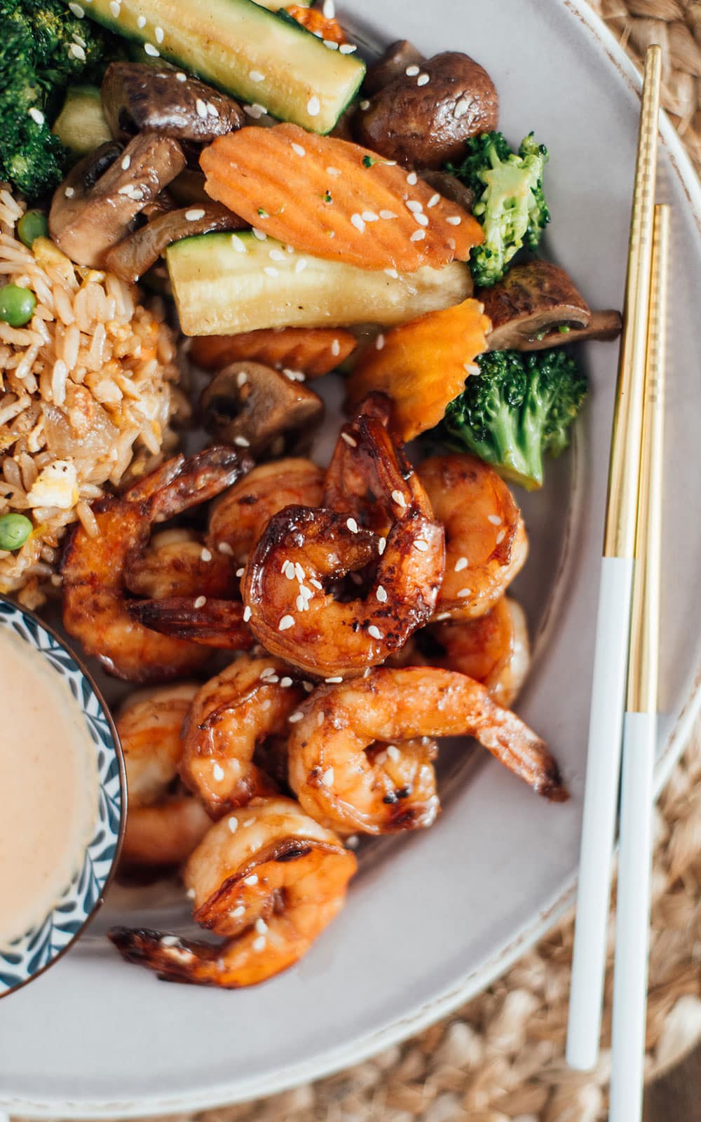 A plate full of hibachi shrimp, hibachi rice and hibachi vegetables with a side of yum yum sauce.