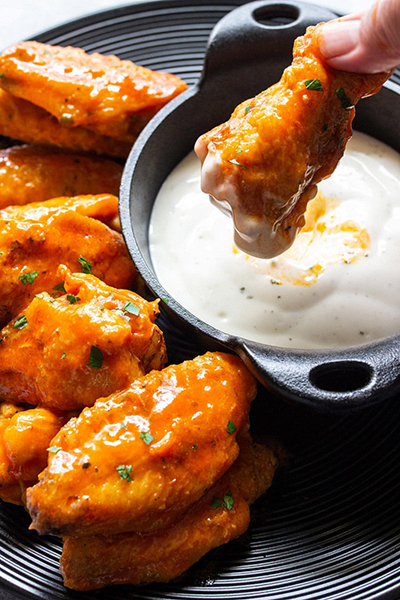 Several air fryer buffalo chicken wings on a black plate with some ranch dressing.