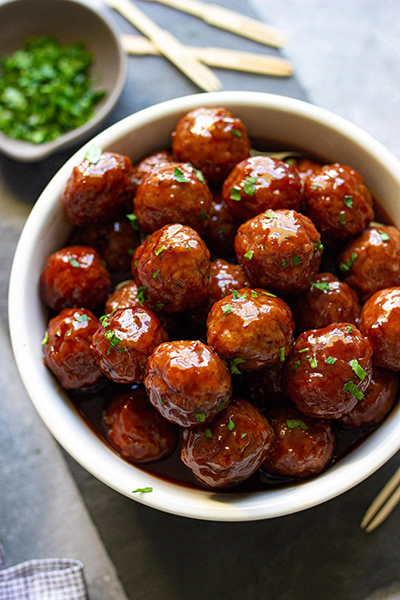 Slow cooker grape jelly meatballs stacked in a white bowl and sprinkled with fresh parsley.