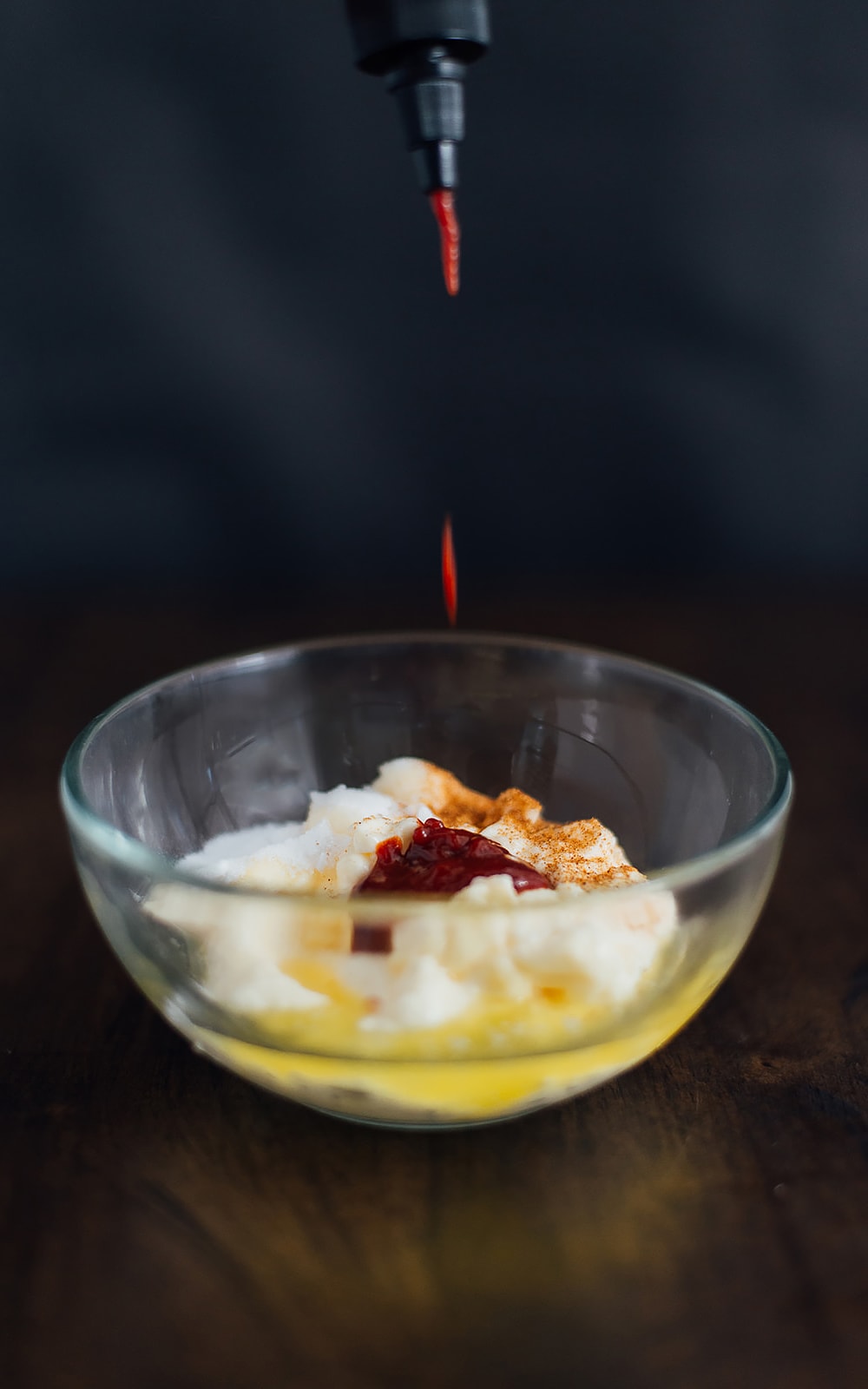 Yum yum sauce in a glass mixing bowl with a drop of Sriracha sauce poured into it.