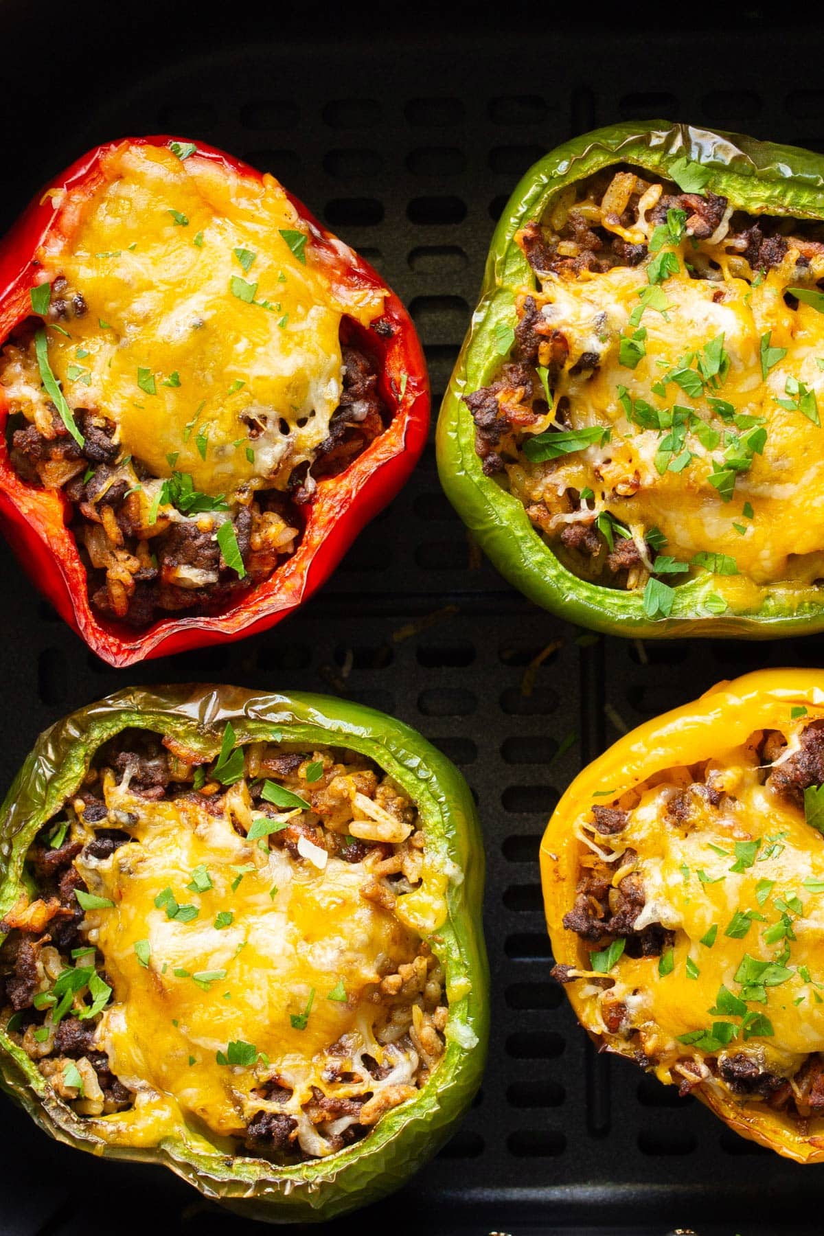 Close up shot of red, green and yellow air fryer stuffed peppers in an air fryer.