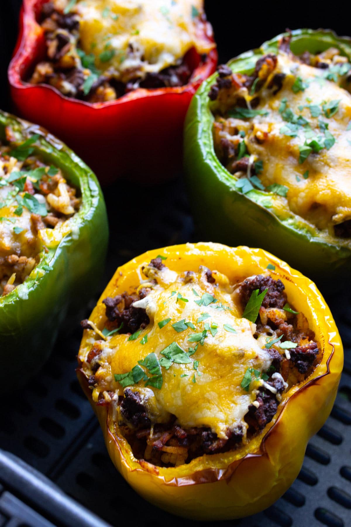 Close up shot of red, green and yellow air fryer stuffed peppers in an air fryer.