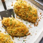 Baked Parmesan crusted chicken on a sheet pan lined with parchment paper.