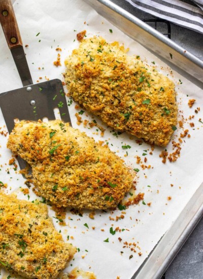 Baked Parmesan crusted chicken on a sheet pan lined with parchment paper.