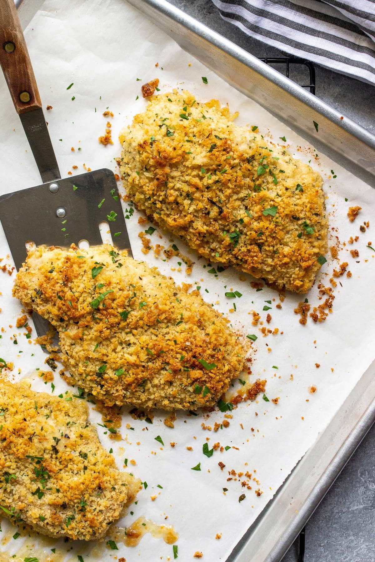 Baked Parmesan crusted chicken on a sheet pan lined with parchment paper.