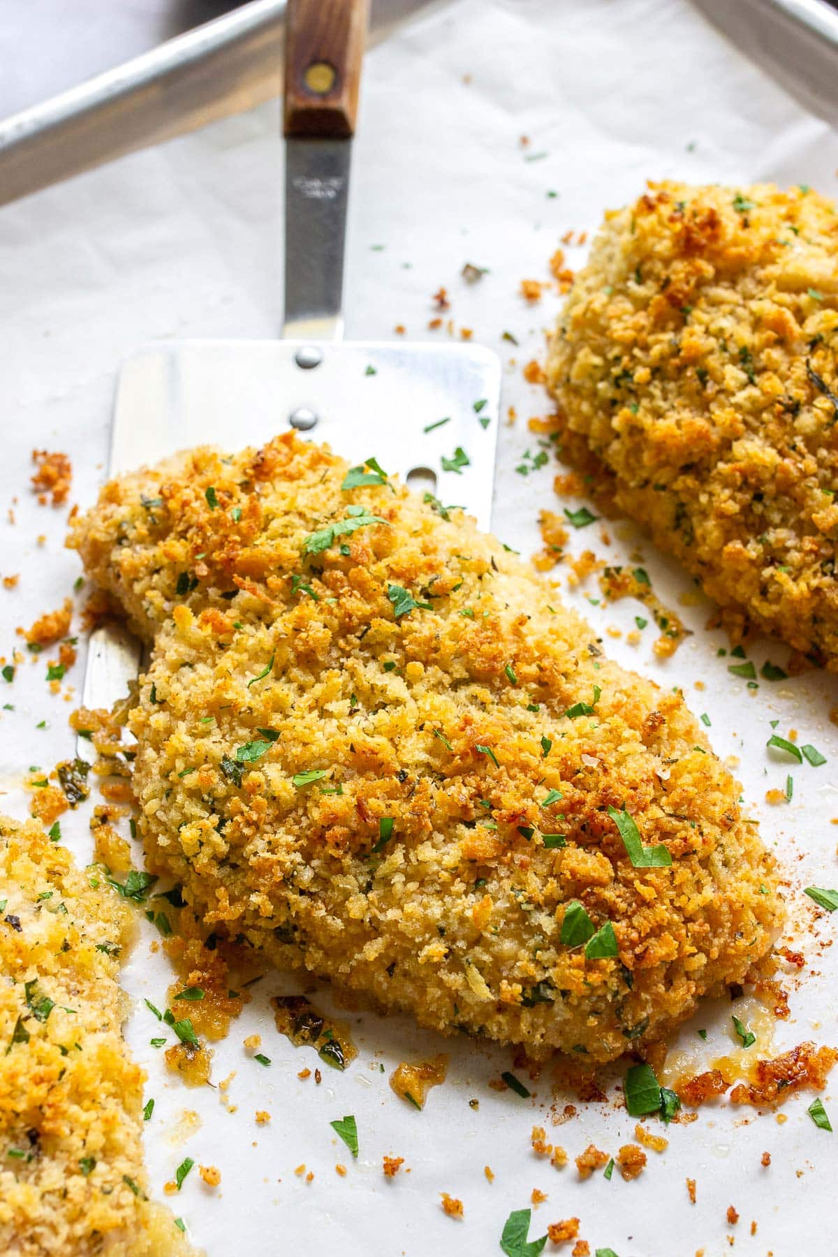 Baked Parmesan crusted chicken on a sheet pan lined with parchment paper.