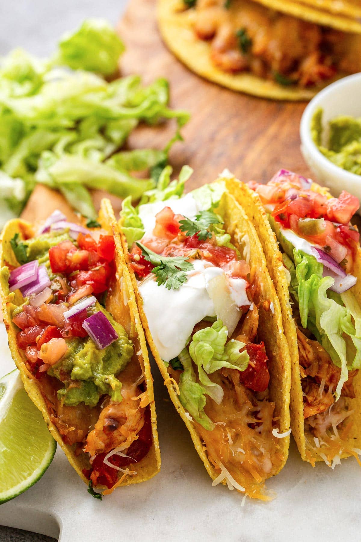 Several cheesy baked chicken tacos stacked together topped with sour cream, tomatos, cilantro, red onions and shredded lettuce.