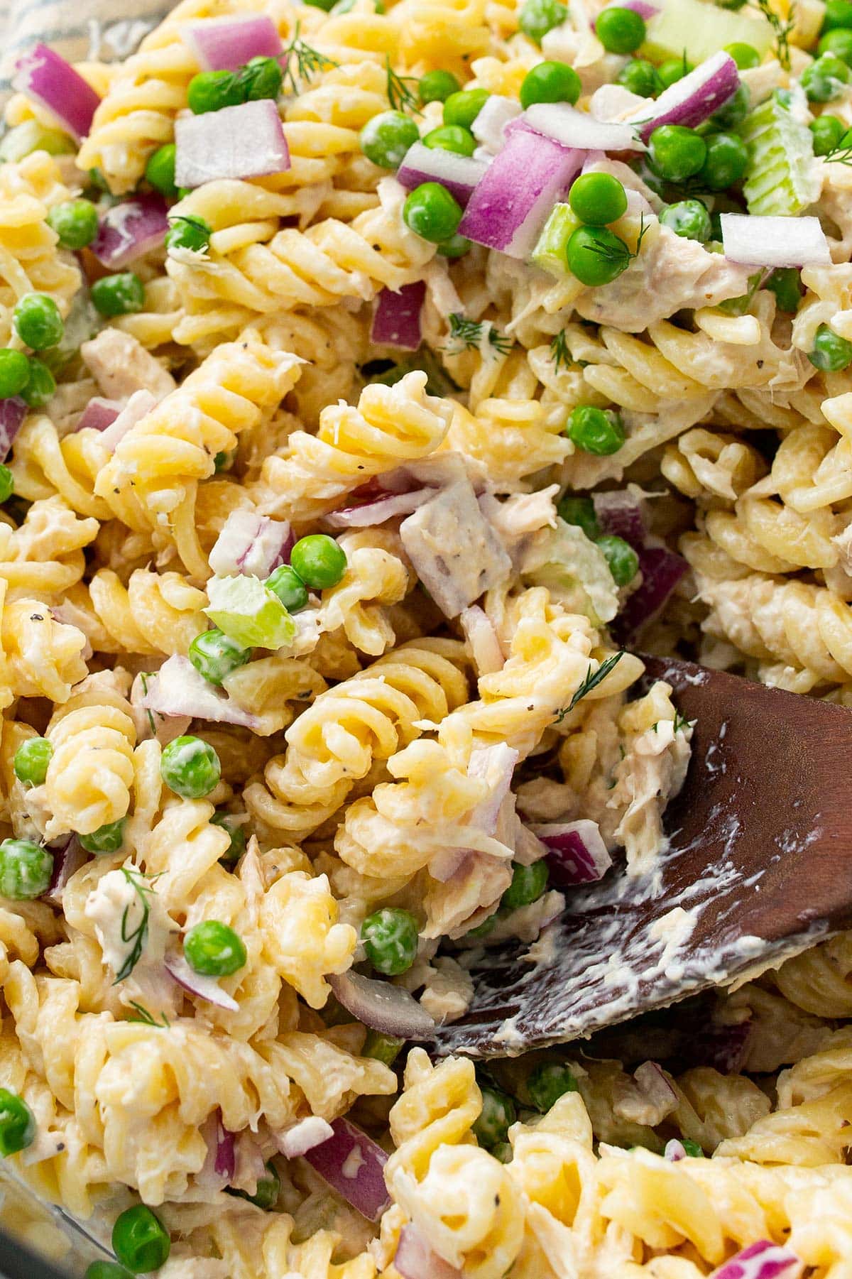 A close up shot of tuna pasta salad with fresh diced red onions, celery, dill and peas.