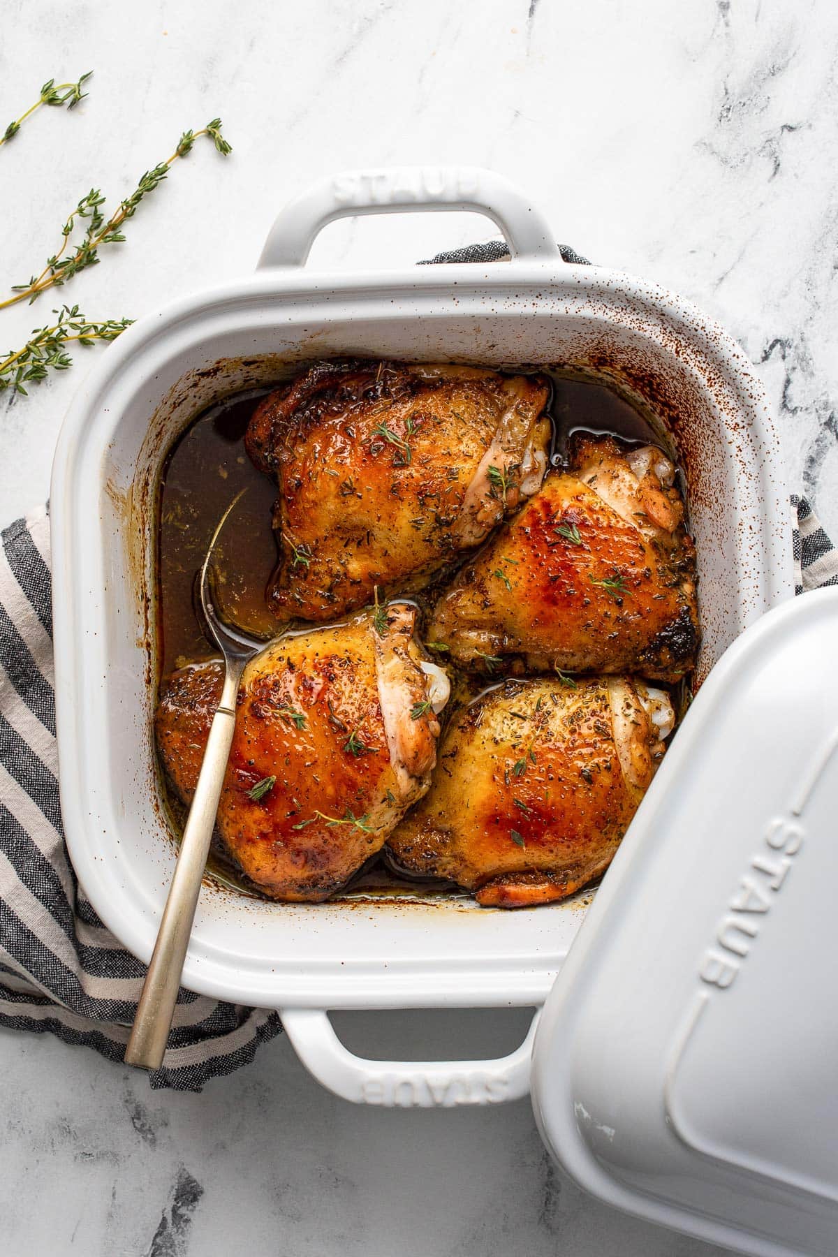 Four honey balsamic chicken thighs with lots of sauce in a white 9x9 baking dish.