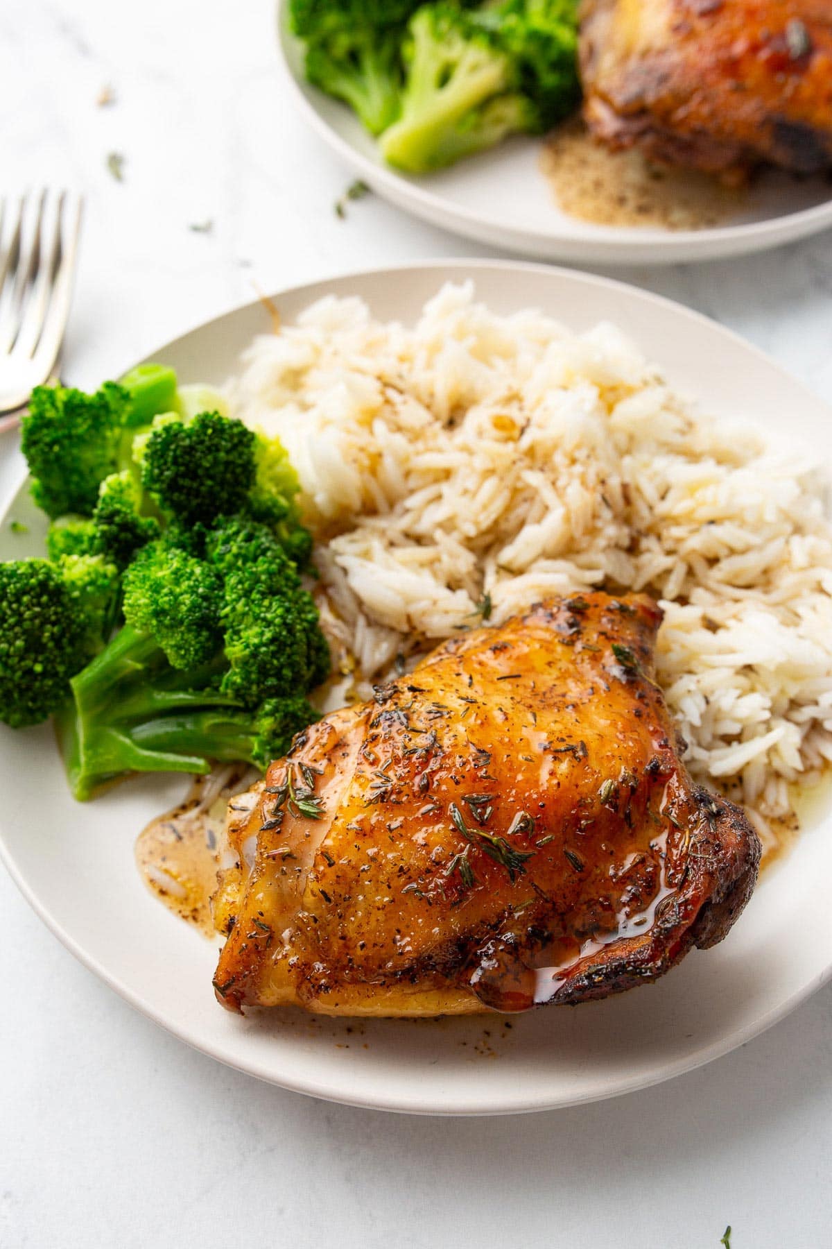 Baked honey balsamic chicken served with white rice and broccoli on two cream-colored plates.
