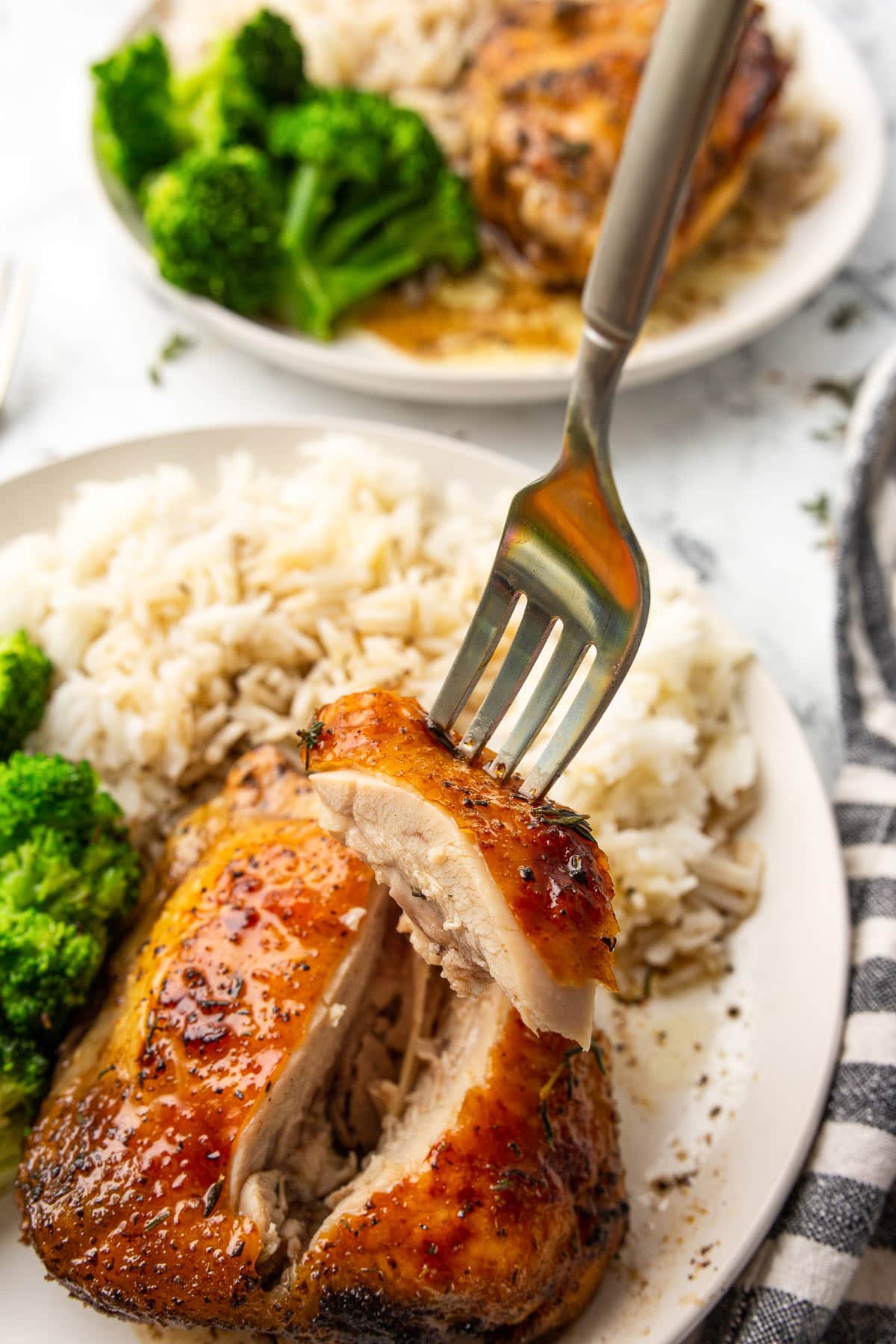 Baked honey balsamic chicken served with white rice and broccoli on two cream-colored plates.