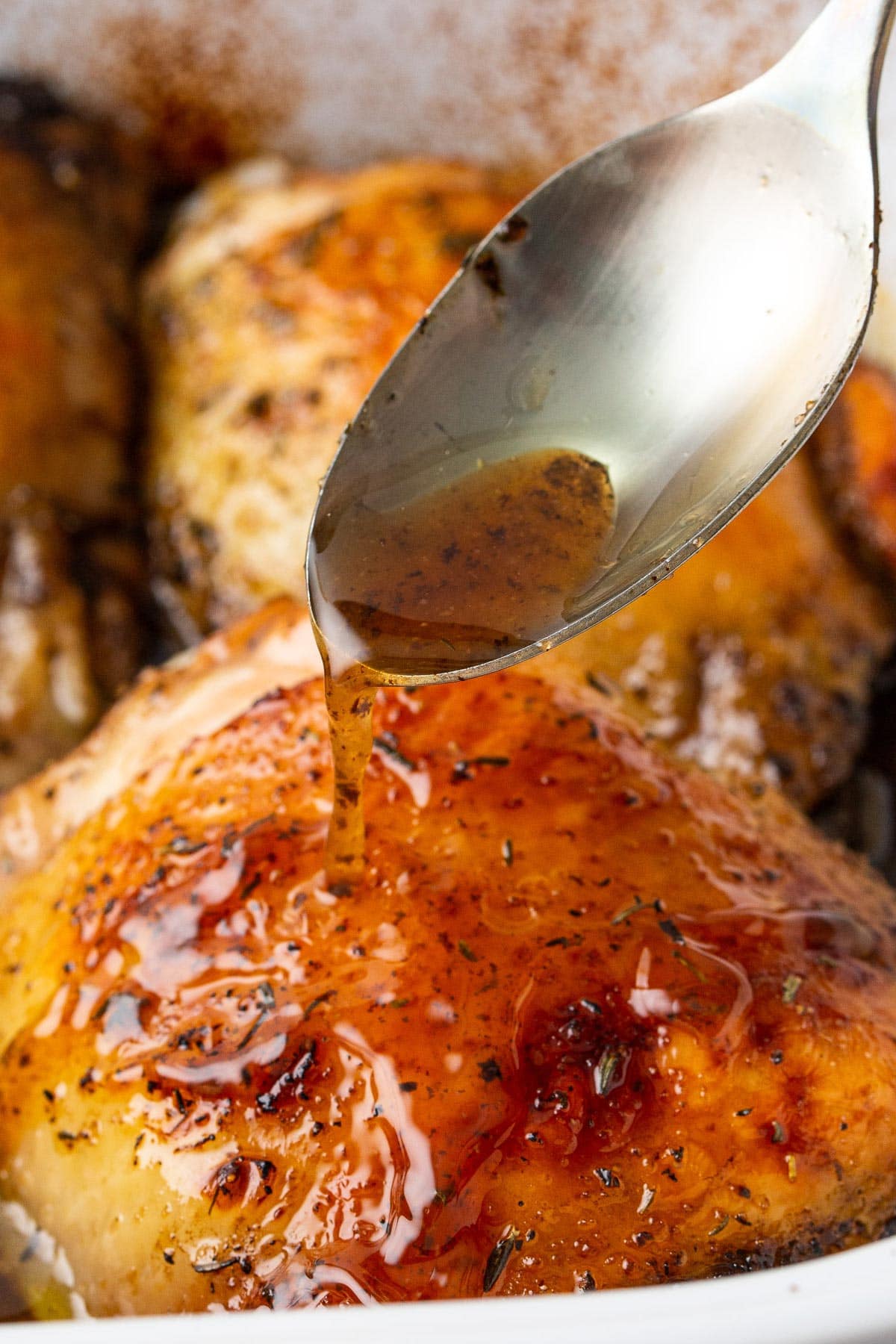 A close up shot of baked honey balsamic chicken with a spoonful of sauce drizzled over it.