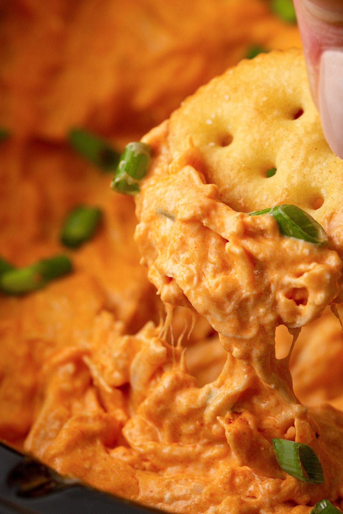 A close up shot of buffalo chicken dip with cheese strings on a Ritz cracker.