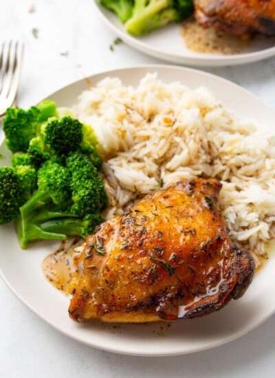 Baked honey balsamic chicken served with white rice and broccoli on two cream-colored plates.