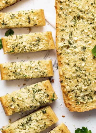 Sliced homemade garlic bread arranged neatly beside a whole loaf of garlic bread.